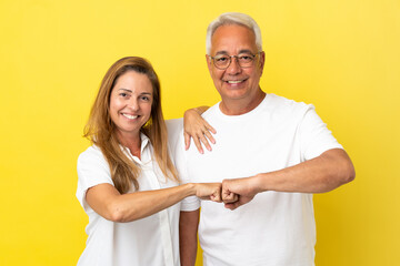 Middle age couple isolated on yellow background bumping fists