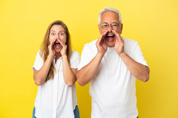 Middle age couple isolated on yellow background shouting with mouth wide open