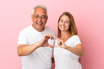 Middle age couple isolated on pink background making a heart with hands