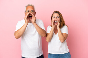 Middle age couple isolated on pink background shouting and announcing something