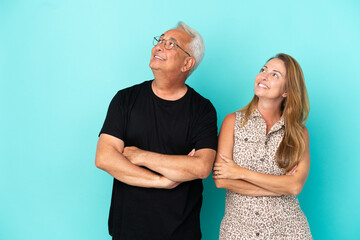 Middle age couple isolated on blue background looking up while smiling
