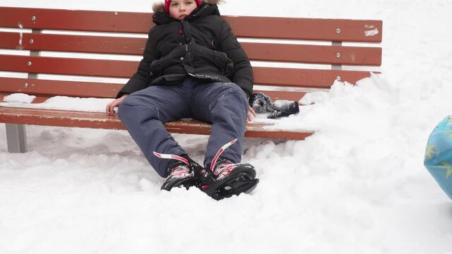 cute caucasian preschooler boy learn to skate on ice rink. Kid wearing winter jacket, hood hat and neckwarmer standing on one knee. Image with selective focus