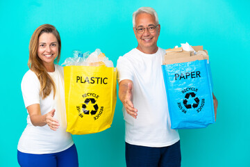 Middle age couple holding a recycling bags full of paper and plastic isolated on white background...