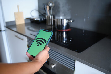 Close up view of a woman using a smartphone app to control her Kitchen Appliances with IOT.