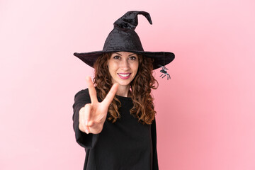 Young caucasian woman celebrating halloween isolated on pink background smiling and showing victory sign