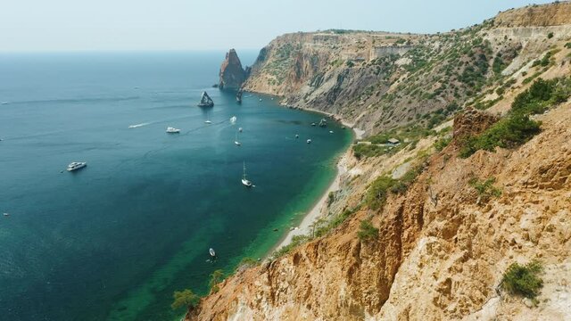 Aerial view of calm azure sea and volcanic rocky cliffs of Mys Fiolent. Pleasure trip boats moored in the bay. Nature summer ocean sea beach background. Holiday, vacation and travel concept