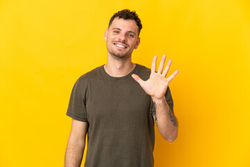 Young caucasian handsome man isolated on yellow background counting five with fingers