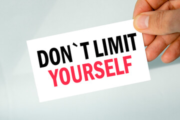 businessman's hand holding paper business card with text dont limit yourself, closeup light gray background