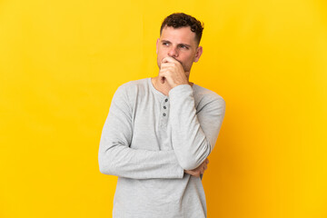 Young caucasian handsome man isolated on yellow background having doubts and with confuse face expression