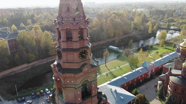 Aerial drone view of bell tower and red-brick cathedral on the background of the river at sunny autumn day. Gethsemane Chernigov Skete, Sergiyev Posad, Russia in 4K