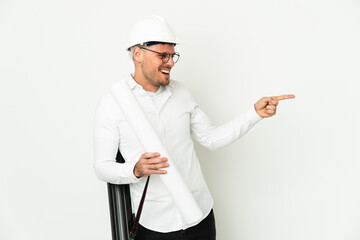 Young architect man with helmet and holding blueprints isolated on white background pointing finger to the side and presenting a product