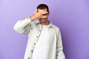 Fototapeta premium Brazilian man over isolated purple background covering eyes by hands and smiling