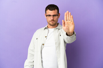Naklejka premium Brazilian man over isolated purple background making stop gesture