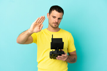 Brazilian man holding a drone remote control over isolated blue background making stop gesture and disappointed