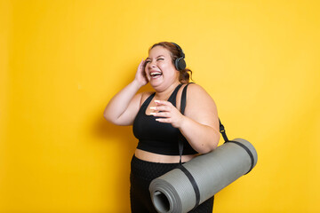 Young plus size fitness woman wearing sportswear listening to music on headphones and laughing out...