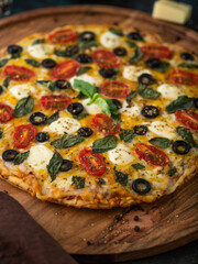 Large pizza topped with cheese olives, tomatoes, mint leaves on a wooden tray. Macro photography. Fast food. Pizzeria, delivery, restaurant, hotel, home cooking.