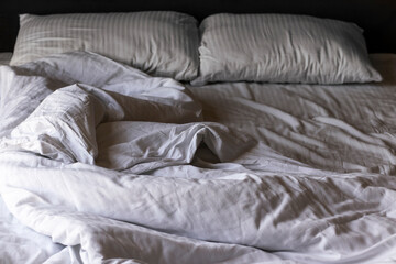 Empty bed with white crumpled linen in the morning. Dark light.