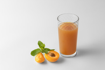 slices of fresh orange apricot with green mint and glass with citrus juice isolated on a white and gray background with natural shadow