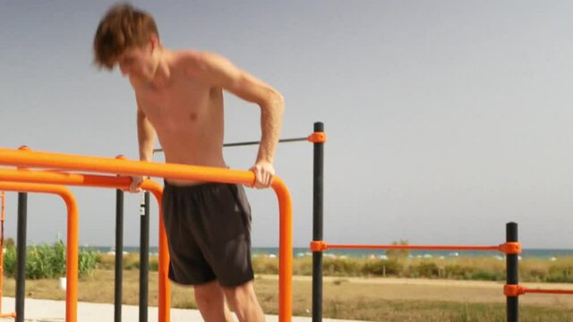 Young blonde man practicing calisthenics on parallel bars.