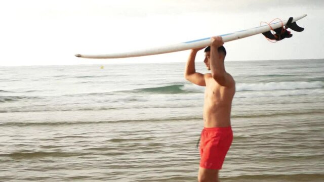 Side view of surfer walking while carrying a surfboard on his head.
