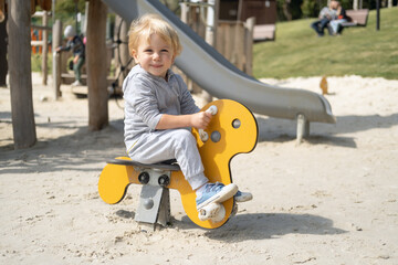 Little caucasian blond boy playing on kids playground in a sunny autumn day