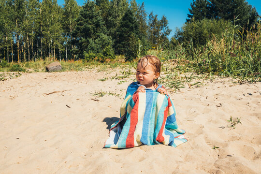 The cute girl sitting after the swimming on the shore of the lake.