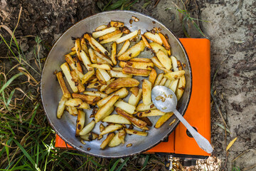 Brown potatoes with onions cooked on a camping gas stove