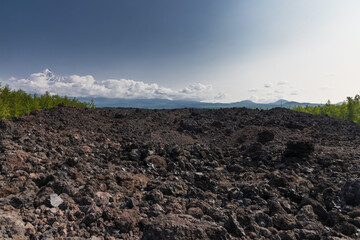 Lava tongue, lava valley, peak of Ostry Tobachik volcano in the clouds in Kamchatka. - obrazy, fototapety, plakaty