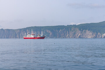 A floating fish-processing plant-ship against the backdrop of the shores of Kamchatka in the Pacific Ocean.