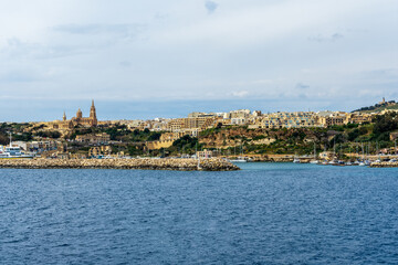 Fototapeta na wymiar Mgarr Harbour and the Chapel of our Lady of Lourde and Ghajnsielem Parish Church.