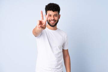 Young Moroccan man isolated on blue background smiling and showing victory sign