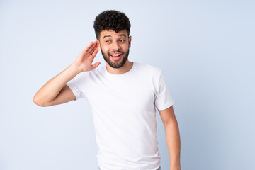 Young Moroccan man isolated on blue background listening to something by putting hand on the ear