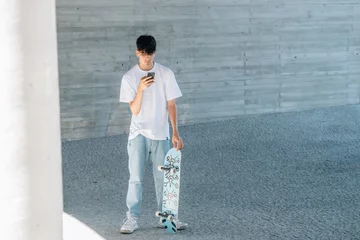 Fotobehang teenage boy with skateboard and mobile phone on the street © carballo