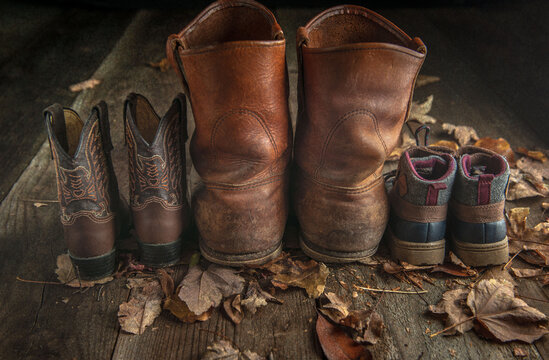 old work boots and childrens boots in fall leaves on wood floor