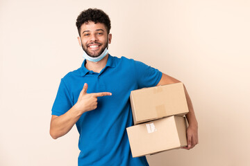 Young delivery Moroccan man isolated on beige background and pointing it