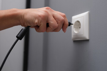 Woman hand inserts electrical plug into outlet closeup