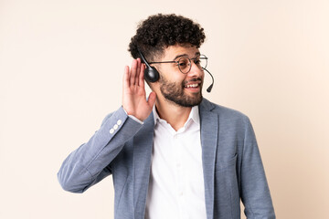 Telemarketer Moroccan man working with a headset isolated on beige background listening to something by putting hand on the ear