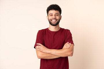 Young Moroccan man isolated on beige background keeping the arms crossed in frontal position