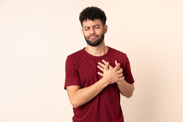 Young Moroccan man isolated on beige background having a pain in the heart
