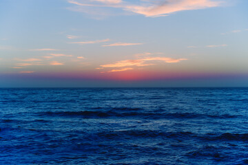 Dark blue water surface background with soft light pink colored cloudy sky. Seascape, no people