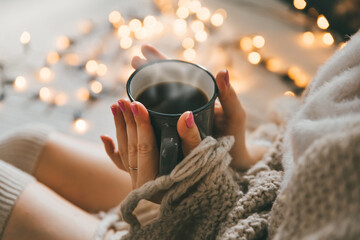 Woman wearing cozy knee socks, sweater and knitted blanket, holding cup of hot coffee on cold winter day