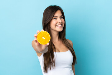 Teenager Brazilian girl over isolated blue background holding an orange
