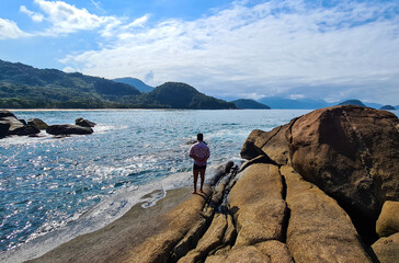 Praia com água cristalina no litoral paulista e homem olhando a praia