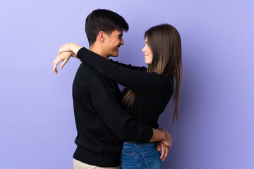 Young couple over isolated purple background hugging
