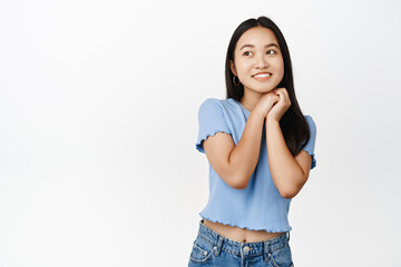 Dreamy brunette asian girl thinking, yearning for something, smiling and gazing aside, standing over white background