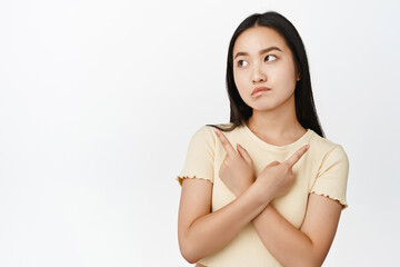Obraz premium Indecisive brunette girl makes tough decision, pointing sideways and looking confused, picking from choices, standing over white background