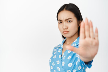Close up of serious asian woman stretch out hand and say no, stop something bad, prohibit action,...