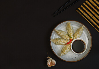 A gyoza dumplings with soy sauce on a gray plate. On a black background with chopsticks. Top view, copy of the space, horizontal