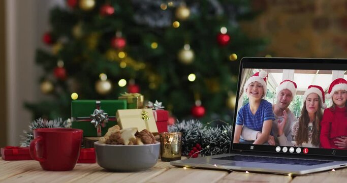 Happy family wearing snata hats on video call on laptop, with christmas decorations and tree