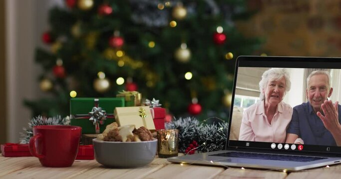 Caucasian senior couple waving on video call on laptop, with christmas tree